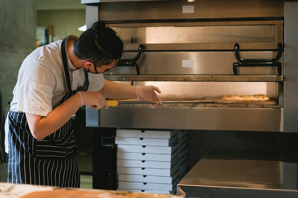 The chef is putting the pizza in the oven.