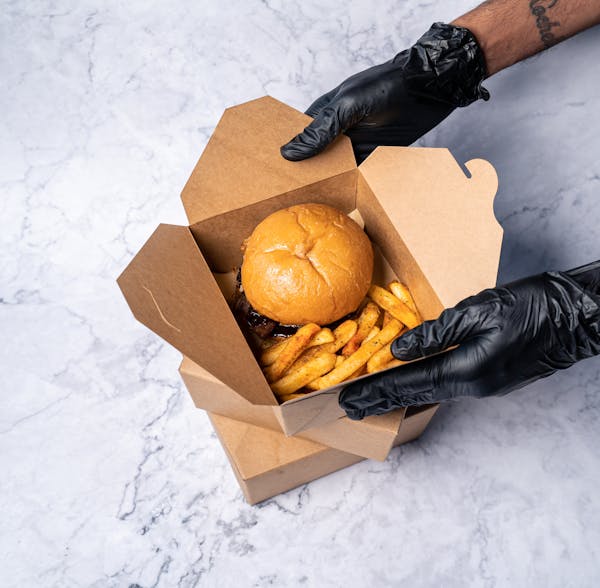 Burger and fries are being packed in disposable takeout container. 