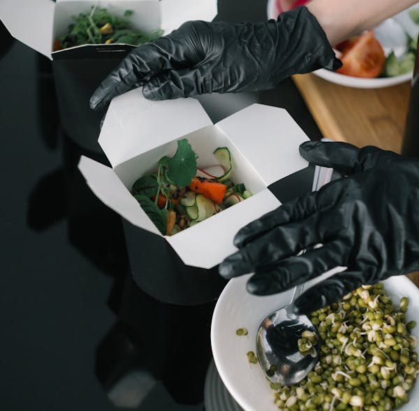 Salad being prepared in a disposable takeout container.