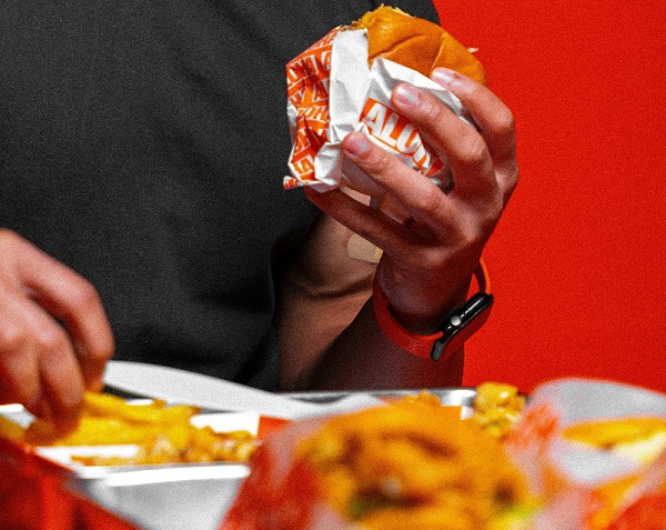 Customers eating burgers in paper packaging at a fast food restaurant.