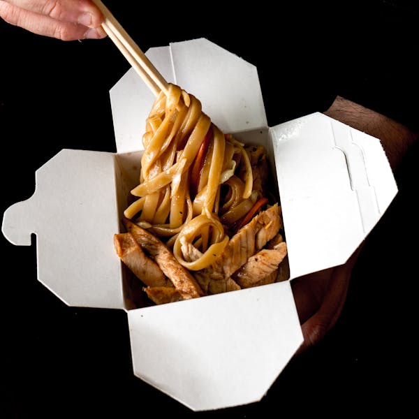 Chopsticks and noodles in disposable takeout container.