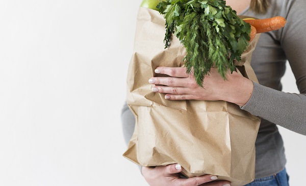 close up woman holding sustainable paper bag with vegetables