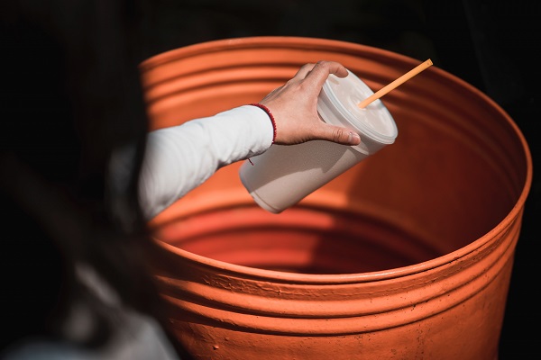 A man is throwing used up disposable foam cups into the trash.